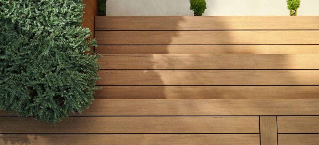Detail PVC terasy s prkny v dřevodekoru a zelení v moderním exteriéru.