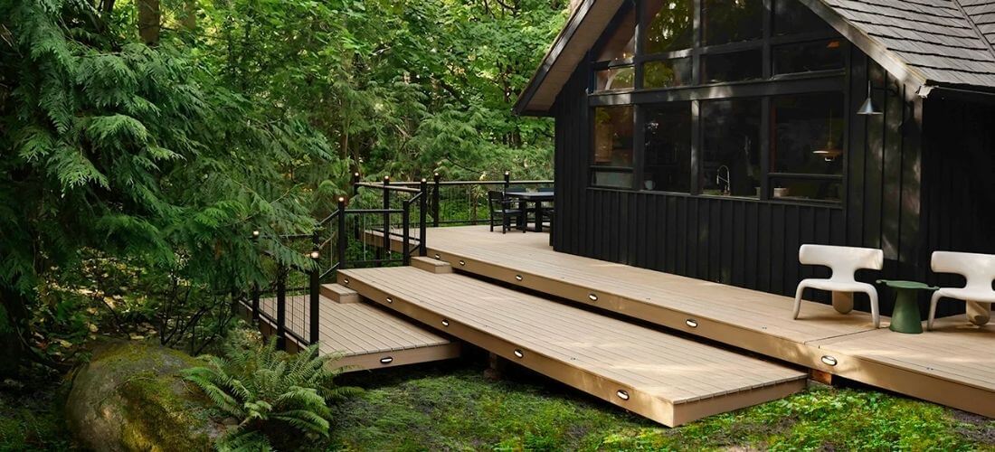 PVC terasa TimberTech Weathered Teak u tmavé fasády v lesním prostředí